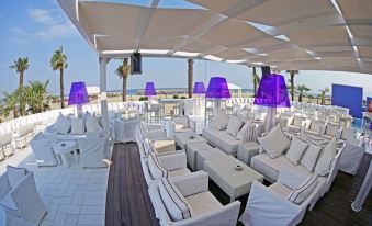 a luxurious outdoor lounge area with white furniture , wooden decking , and purple lights , overlooking the ocean at Mediterranean Village Hotel & Spa