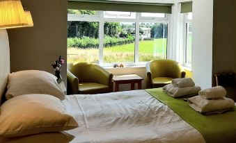 a bedroom with a large bed , two chairs , and a window overlooking a grassy field at The White House Guest House