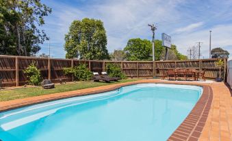 an outdoor swimming pool surrounded by a wooden fence , with several lounge chairs placed around the pool area at Maffra Motor Inn