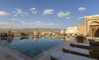 a large outdoor swimming pool surrounded by lounge chairs and a mountain in the background at Kayakapi Premium Caves Cappadocia