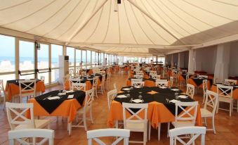 a large dining room with white tables and chairs , black tablecloths , and a dining table set for a meal at La Plage Resort