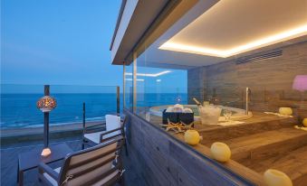 a modern living room with a glass wall , overlooking the ocean , and a wooden deck with a hot tub at Hotel Meridional