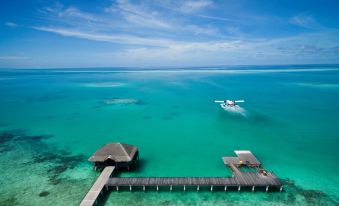 aerial view of a boat floating in the ocean near a pier , surrounded by clear blue water at Medhufushi Island Resort