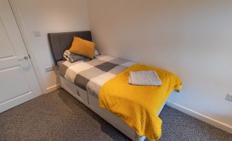 a neatly made bed with a gray headboard and yellow pillows , topped with a white blanket and a square pillow at Scenic Roots