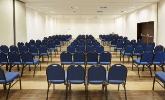 a large conference room with rows of blue chairs and white walls , ready for an event at Tulip Inn Itaguai