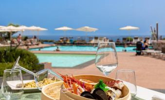 a table with a bowl of food , wine glass , and cocktail is set up near a pool at Domina Zagarella Sicily