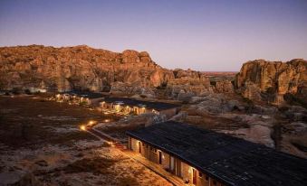 a beautiful mountainous landscape at dusk , with a group of buildings illuminated by lights and surrounded by rocks at Isalo Rock Lodge