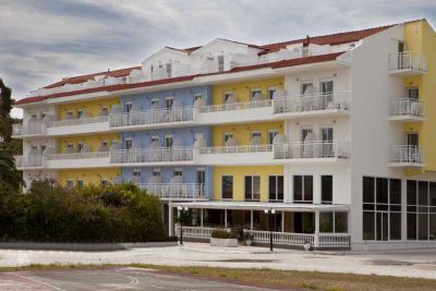 a yellow and blue apartment building with multiple balconies , situated next to a road and surrounded by trees at Hotel Summery