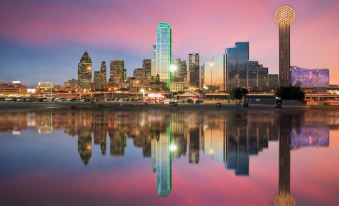 a city skyline at sunset , with tall buildings lit up and a calm body of water reflecting the scene at Thunderbird Motel Hillsboro