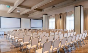 an empty conference room with rows of white chairs and two large screens on the walls at Doubletree by Hilton Brescia