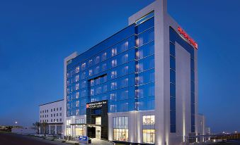 a modern hotel building with a large glass facade and blue lights at night , standing on a street with a city street in front of it at Hilton Garden Inn Tabuk