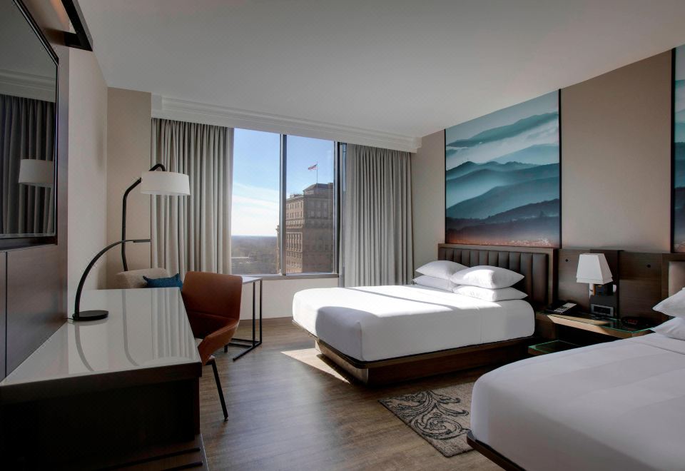 a modern hotel room with two beds , a desk , and a large window offering a view of the city at Winston-Salem Marriott