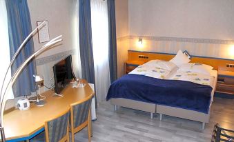 a hotel room with a blue and white bed , desk , chair , and a tv . also a bed in the room at Hotel Restaurant Post Italia