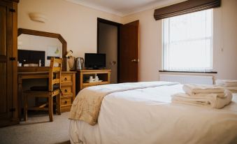 a neatly made bed with a beige blanket is in a room with a wooden desk , computer monitor , and a window at The Stratton House Hotel