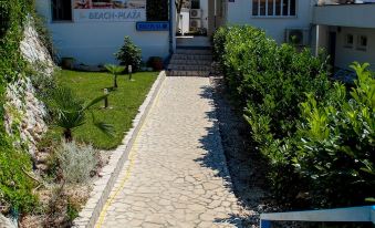 a paved walkway surrounded by a white building , with bushes and trees lining both sides of the path at Beach Hotel