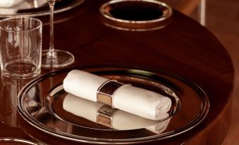 a silver plate with a white napkin on it , placed on a wooden table next to a wine glass at Cap d'Antibes Beach Hotel