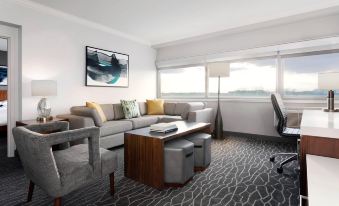a modern living room with a gray couch , wooden coffee table , and chairs , along with large windows at Delta Hotels Woodbridge