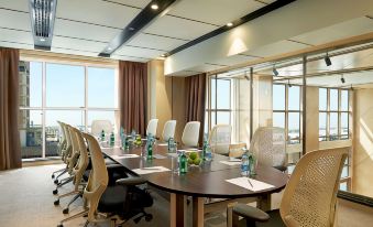 a conference room with a wooden table surrounded by white chairs and water bottles on the table at Hilton Garden Inn Al Jubail