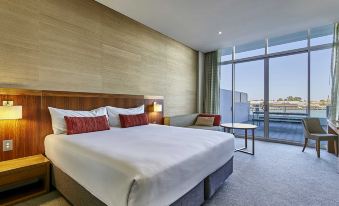 a large bed with white linens is in a hotel room with a view of the ocean at The Sebel Mandurah