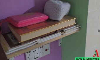 a stack of books , a heart - shaped object , and a pink bag are placed on a shelf at Adamson Inn Penang