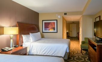 a hotel room with two beds , a nightstand , and a door leading to another room at Hilton Garden Inn Kennett Square