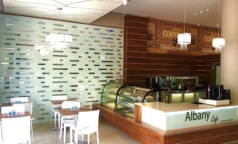 a modern coffee shop with a wooden counter , white tables and chairs , and a glass display case at Albany Hotel