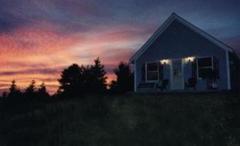 a small blue house is lit up at night with a beautiful sunset in the background at Chisholms of Troy Coastal Cottages
