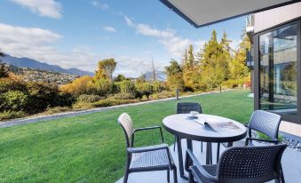 a patio area with a table and chairs set up for outdoor dining , surrounded by green grass and trees at Oaks Queenstown Shores Resort