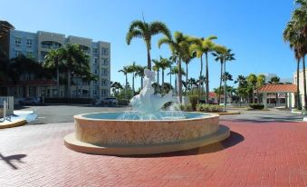 a large white fountain in the middle of a red brick plaza , surrounded by palm trees at Aquarius Vacation Club at Boqueron Beach Resort