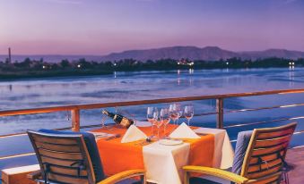 a romantic dinner setting on a boat , with a bottle of wine placed on a table and wine glasses nearby at The Oberoi Zahra, Luxury Nile Cruiser