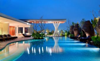 a large swimming pool surrounded by palm trees , with a house in the background and a building nearby at Hilton Bandung