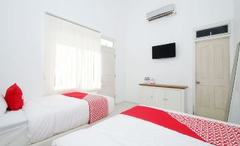 a white bedroom with two beds , one on the left and one on the right side of the room at Griya RW Family Guest House Redpartner