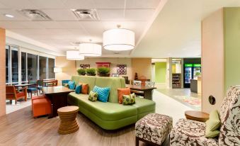 a modern and stylish lounge area with green sofas , wooden flooring , and pendant lights , providing an inviting atmosphere for relaxation at Home2 Suites by Hilton Omaha/West