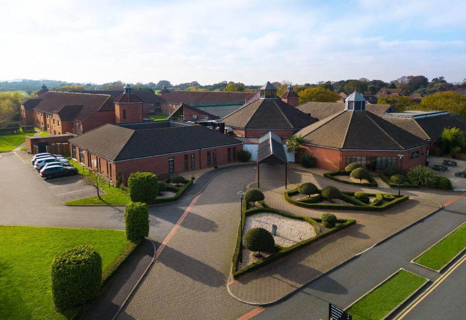 aerial view of a large brick building surrounded by grass and trees , with a park in front of it at Delta Hotels Waltham Abbey