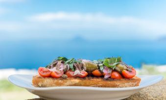 a white plate with a sandwich topped with tomatoes , cucumbers , and onions sits on a dining table at Hotel Ravesi