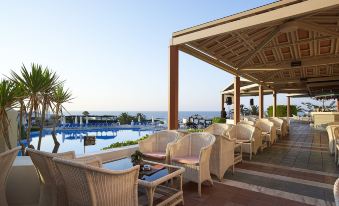 a resort with a pool surrounded by lounge chairs and tables , overlooking the ocean at Aldemar Knossos Royal