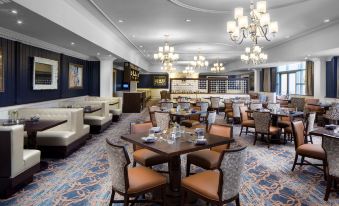 a large dining room with multiple tables and chairs , a bar area , and a chandelier at Desmond Hotel Malvern, a DoubleTree by Hilton