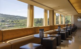 a room with wooden walls and large windows overlooking a valley , featuring several black leather chairs and tables at Hotel Fundador