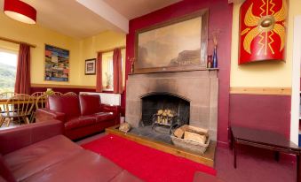 a cozy living room with a fireplace , red couches , and a painting on the wall at YHA Eskdale