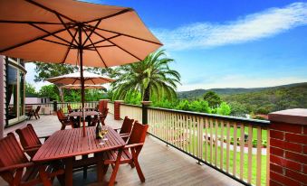 a wooden deck with multiple dining tables and chairs , surrounded by trees and overlooking a valley at Hotel Bellinzona Daylesford