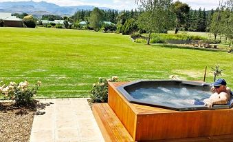 a wooden deck with a hot tub on it , surrounded by lush greenery and a grassy field at Country Comfort