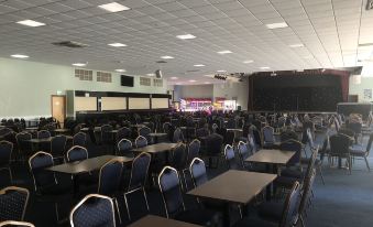 a large dining area with multiple tables and chairs , a stage at the end , and screens on the wall at North Devon Resort