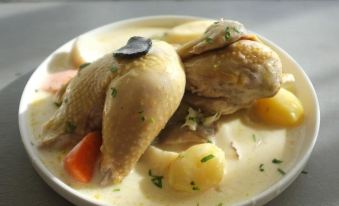 a white plate with a bowl of chicken on it , accompanied by a fork and knife at La Maison Navarre