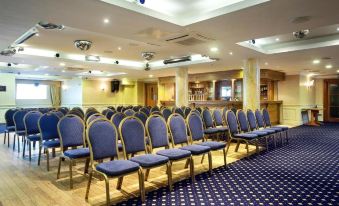 a conference room with rows of blue and gold chairs , a bar in the background , and recessed lighting at Tara Hotel