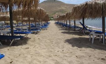 a row of lounge chairs under straw umbrellas on a sandy beach , with a mountain in the background at Villa Victoria