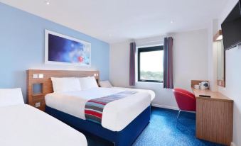 a modern hotel room with blue walls , white bed linens , and red telephone , along with a window offering a view of the city at Travelodge Wincanton