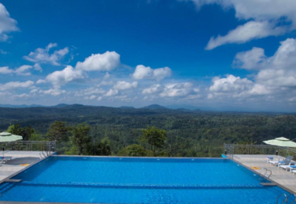 a large outdoor swimming pool surrounded by lush greenery , with a beautiful view of the mountains in the distance at Coorg Cliffs Resort