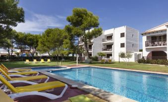 a swimming pool with yellow lounge chairs and umbrellas , surrounded by buildings and trees under a clear blue sky at Sol Y Mar