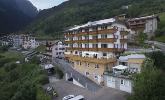 a large , multi - story building with balconies and balconies of various shapes and colors is situated in a mountainous area at Hotel Olympia