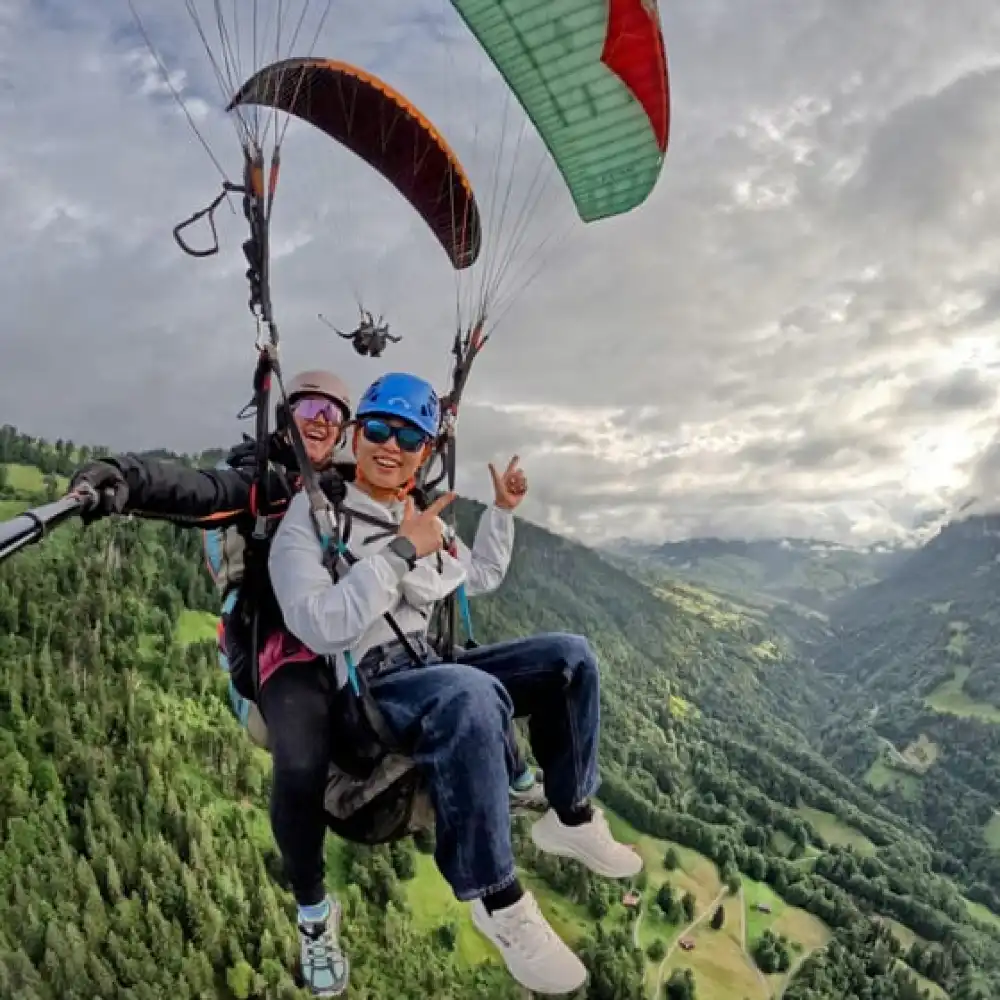 Paralayang tandem terbang di atas Batu Malang dengan pemandangan perbukitan hijau dan lembah yang mengelilingi kota